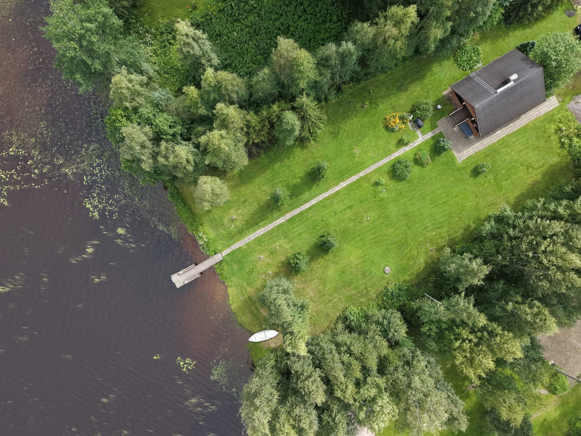 Ilmakuva mökkirannasta: mökki, laattapolku, laituri ja vene